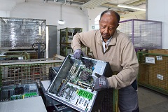 Ein Mann steht vor Kisten mit Elektroschrott und hält einen alten Computer in den Händen